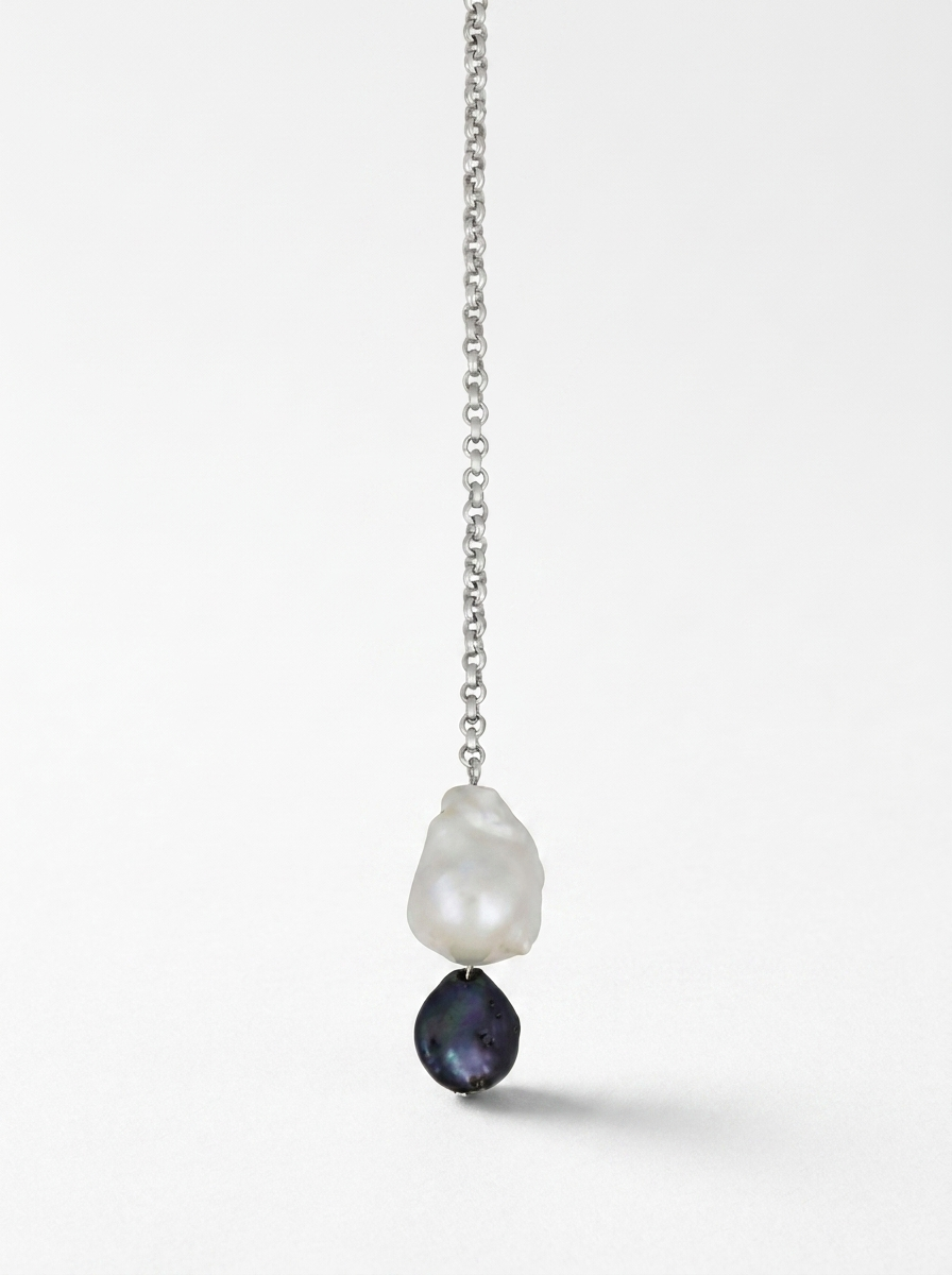 Close-up of a choker with a long chain and two pearls, one white and one black
